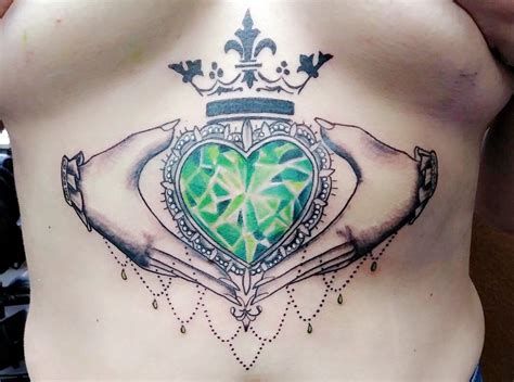 a woman's stomach with a green heart and two hands holding a crown on it