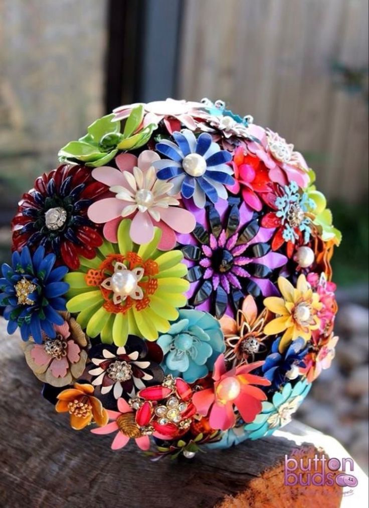 a colorful flower brooch sitting on top of a piece of wood next to a fence