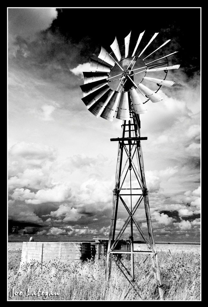 black and white photograph of a windmill in the middle of a field with clouds overhead