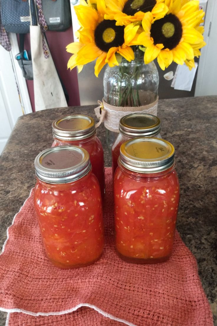 three jars filled with jam sitting on top of a table next to sunflowers