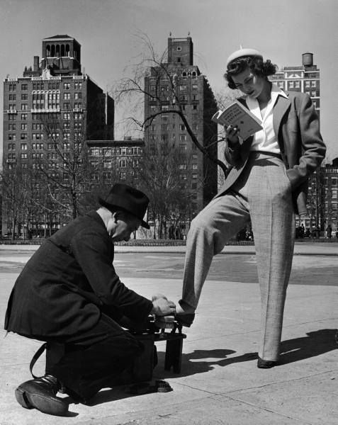 an old photo of a man sitting on a bench with a woman standing next to him