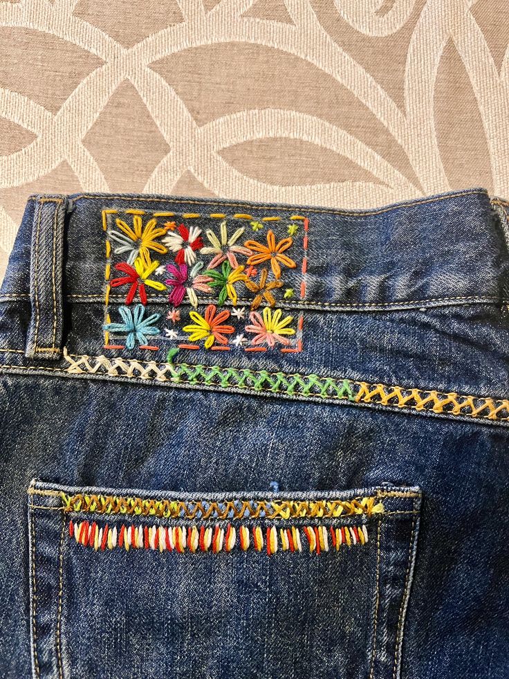 the back pocket of a pair of blue jeans with embroidered flowers on them and beaded trimmings