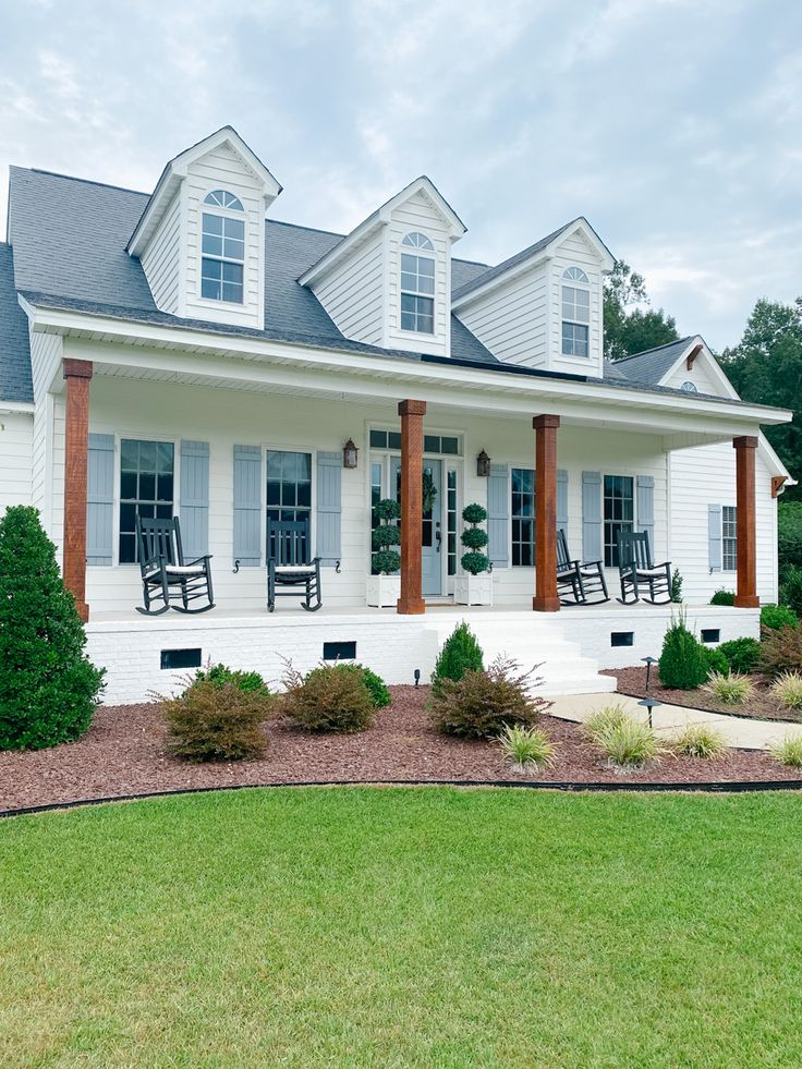 a white house with porches and chairs on the front lawn