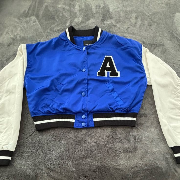 Never Worn Trendy Blue Varsity Jacket For Streetwear, Blue Buttoned Outerwear For Streetwear, Trendy Outerwear With Buttons For College, Blue Varsity Jacket With Button Closure For College, White Cotton Varsity Jacket With Button Closure, Blue College Varsity Jacket With Button Closure, College Blue Varsity Jacket With Button Closure, Trendy Blue College Varsity Jacket, Spring Varsity Jacket With Button Closure