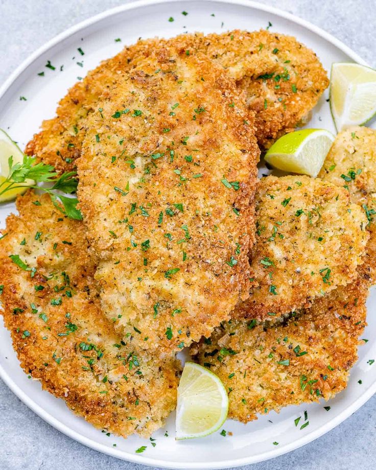 two fried chicken patties on a white plate with lemon wedges and parsley