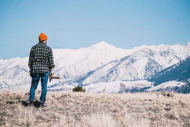 a man standing on top of a dry grass covered field next to snow covered mountains