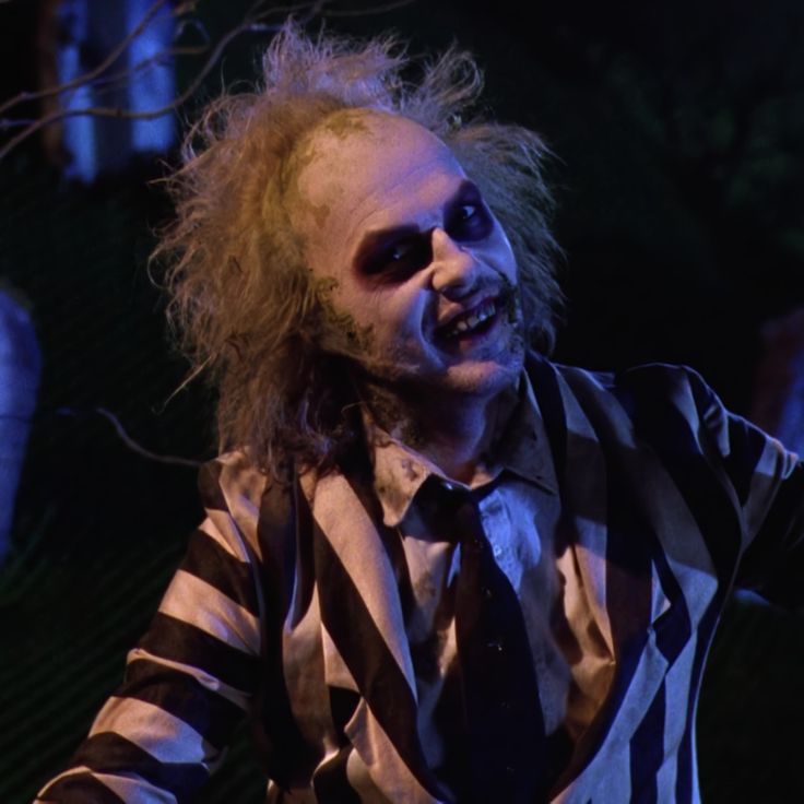 a man dressed as the joker in a striped shirt and tie with his hands out