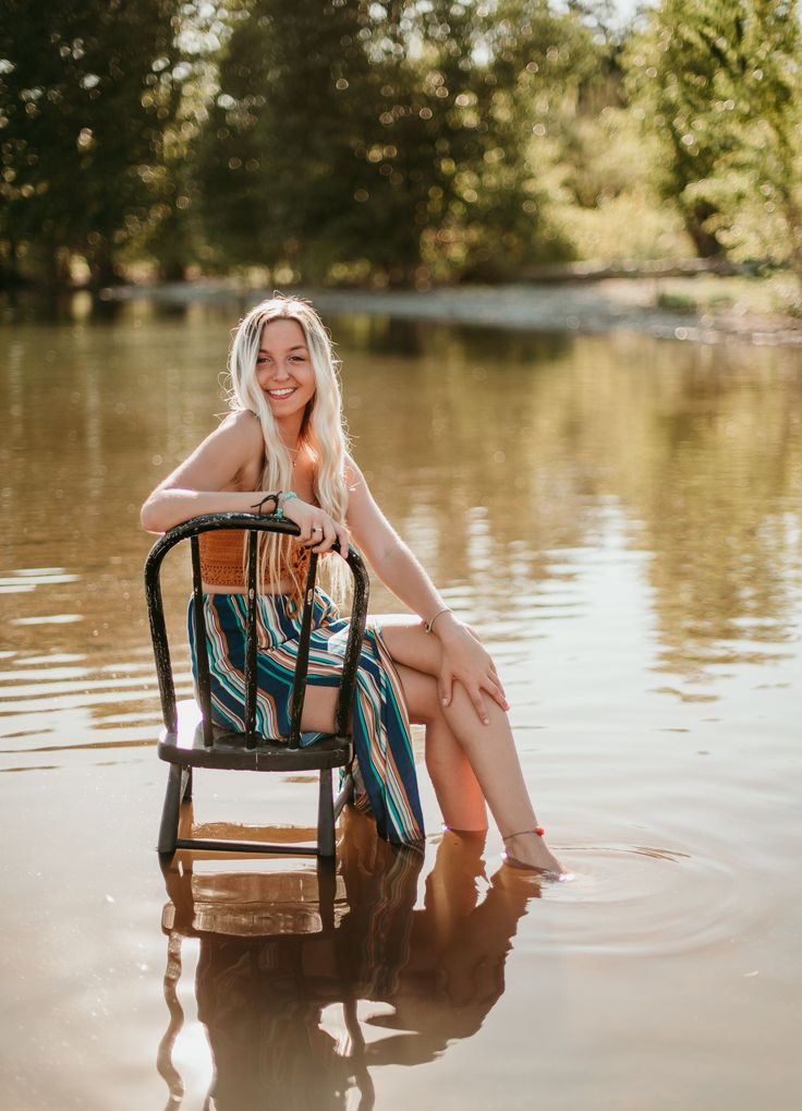 a woman sitting in a chair on top of a body of water with trees in the background