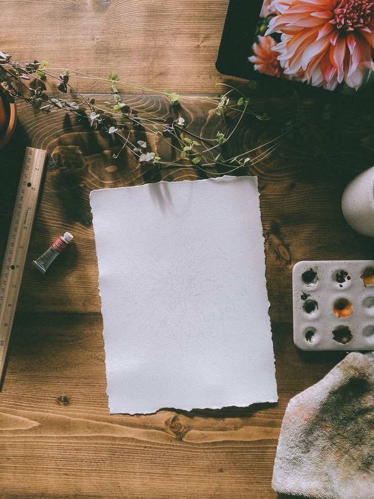 a piece of paper sitting on top of a wooden table next to a ruler and flowers