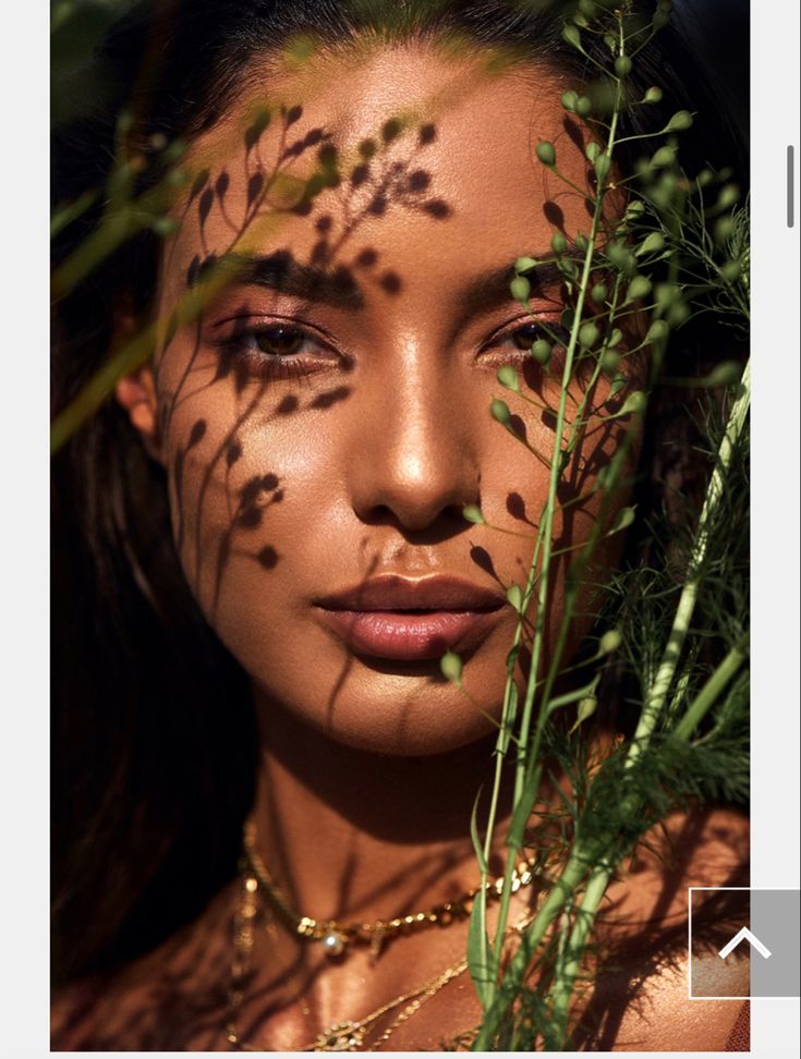 a woman with leaves on her face and chest is surrounded by greenery as she poses for the camera