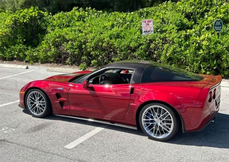 a red sports car parked in a parking lot next to some bushes and shrubbery