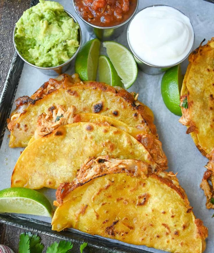 some tacos and guacamole are sitting on a tray with limes