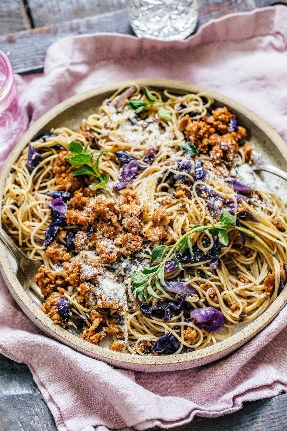 a bowl filled with pasta and meat on top of a pink napkin next to a glass of water