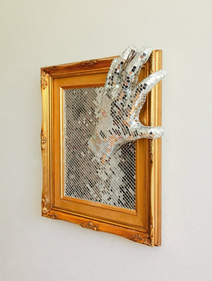 a gold frame with a hand made out of silver sequins hanging on the wall