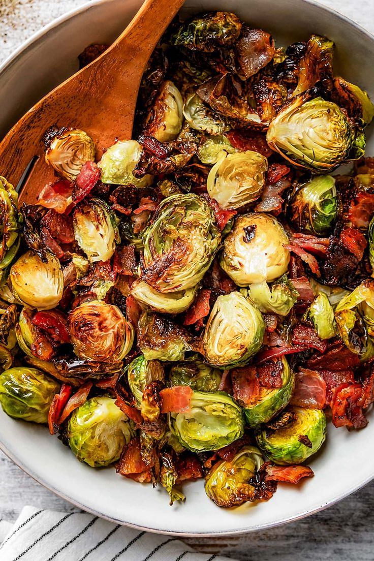 brussel sprouts and bacon in a white bowl with a wooden spoon