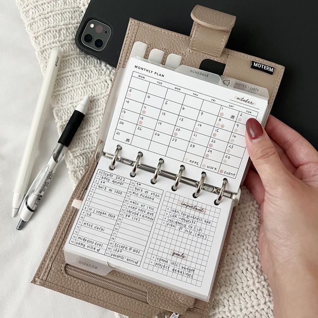 a person is holding a planner in front of a cell phone and pen on a white blanket