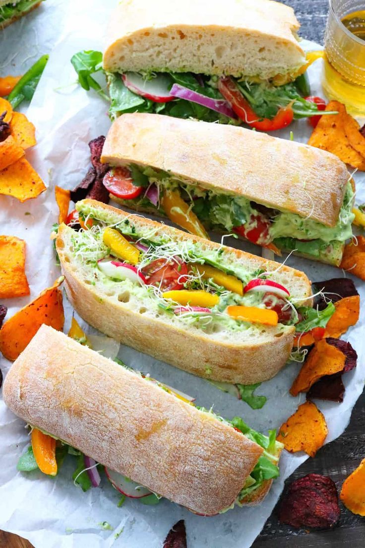 three sub sandwiches with lettuce, tomatoes and other toppings on parchment paper