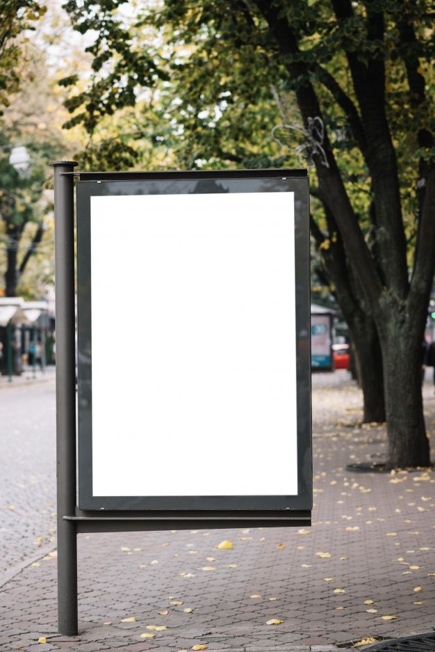 a large white sign sitting on the side of a road next to a tree filled street