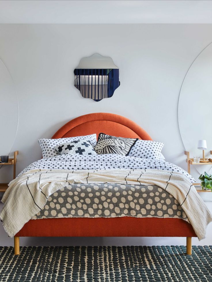 a bed with an orange headboard and pillows on it in a white walled room