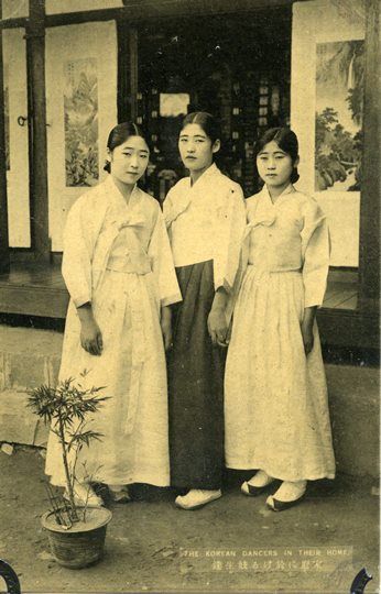 three women standing next to each other in front of a building with a potted plant