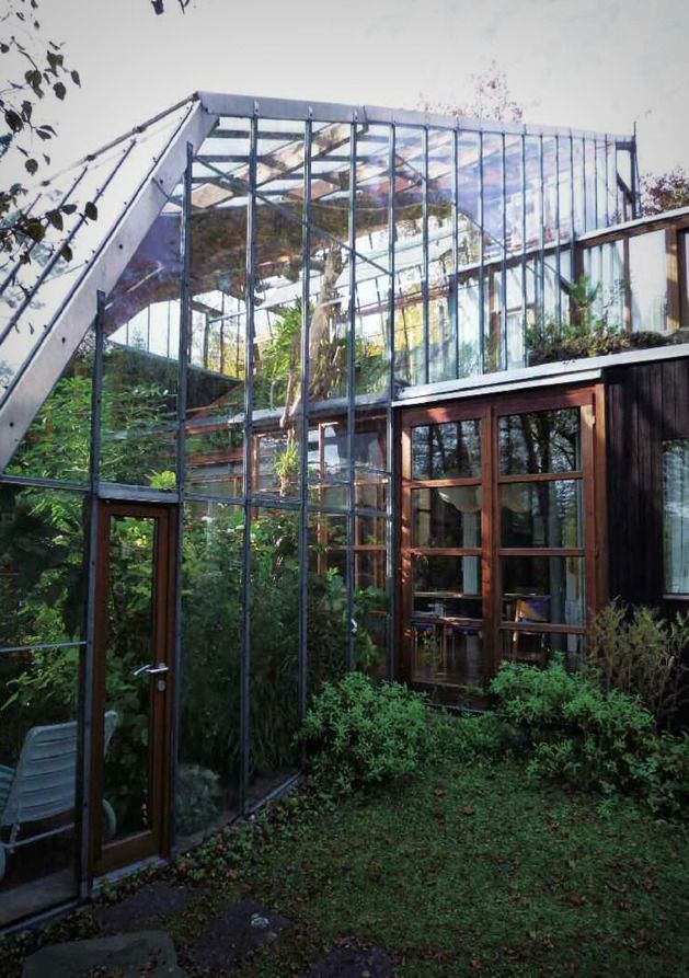 a house with glass walls and lots of plants in the yard next to some stairs