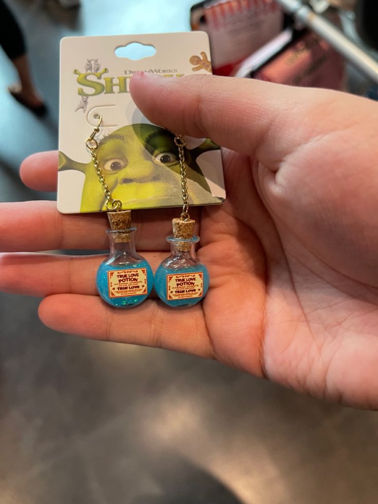 a hand holding two small bottle necklaces in front of a card with an advertisement on it