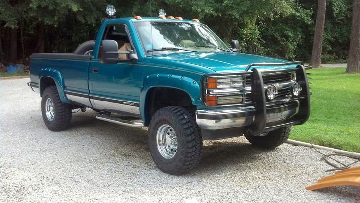 a blue pick up truck parked on the side of a road in front of some trees