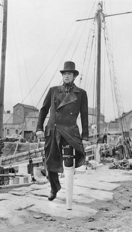 an old photo of a man in a trench coat and hat standing on a dock