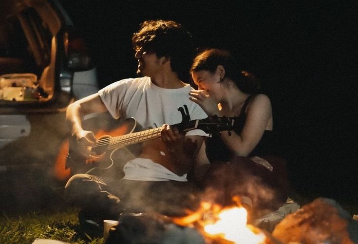 a man and woman sitting next to each other on the ground with a guitar in front of them