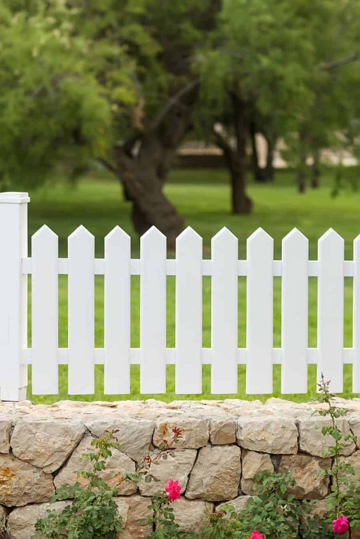 a white picket fence with flowers in the foreground