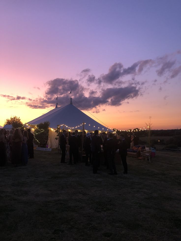 a group of people standing in front of a tent at sunset