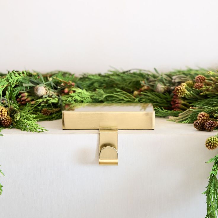 a white table topped with green plants and pine cones next to a gold door handle