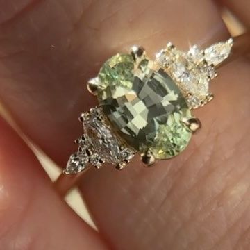 a close up of a person's hand holding a ring with an oval shaped green stone