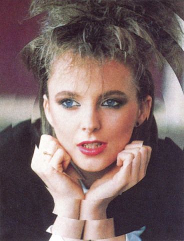 the woman is posing with her hand on her chin and wearing a black jacket, white shirt and blue eyeshadow