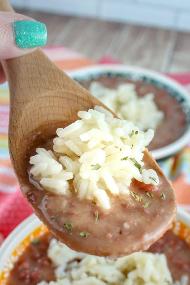 a wooden spoon filled with rice and beans on top of a plate next to another bowl