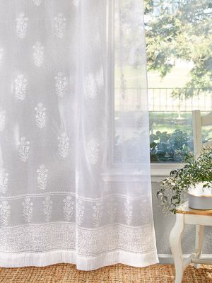 a white curtain hanging in front of a window next to a small table with a potted plant on it