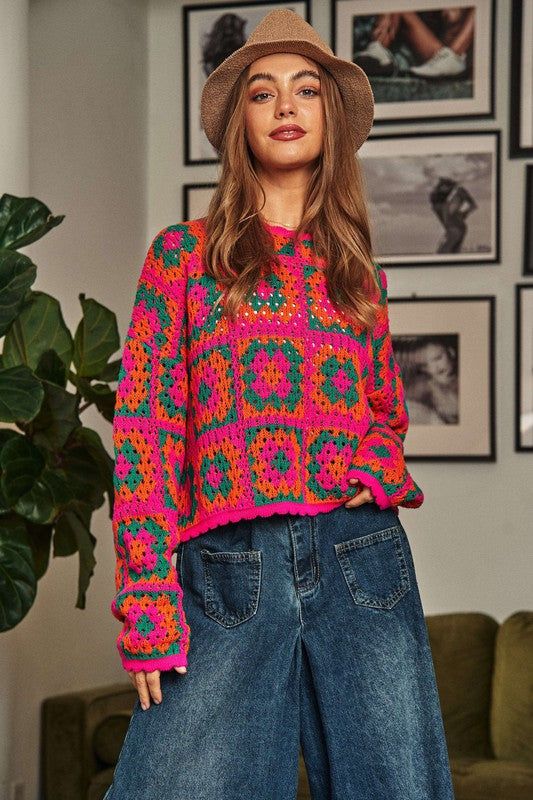 a woman standing in front of a green couch wearing a pink sweater and blue jeans