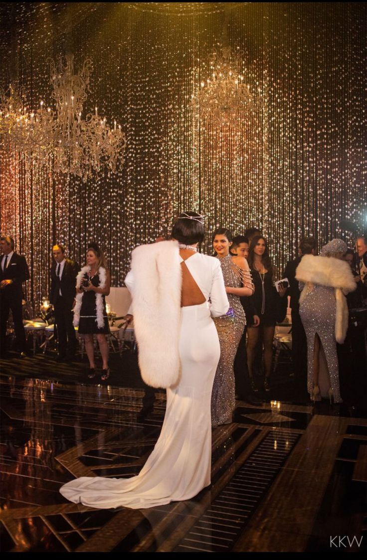 a woman in a long white dress standing next to a man wearing a fur coat