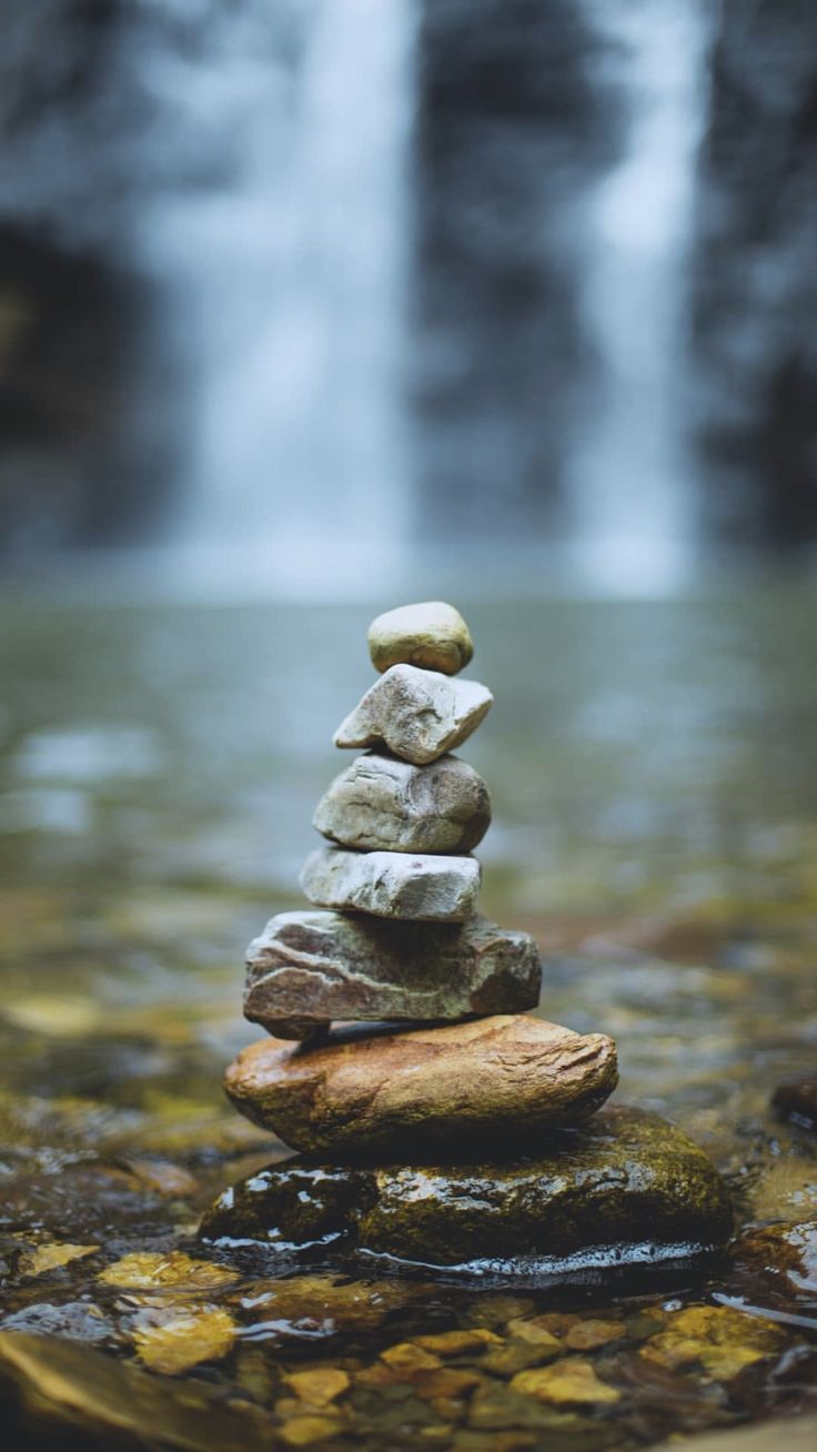 a stack of rocks sitting on top of a river next to a waterfall in the forest