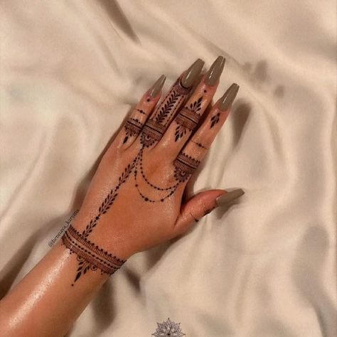 a woman's hand with henna tattoos on her left arm and wrist, resting on a white sheet