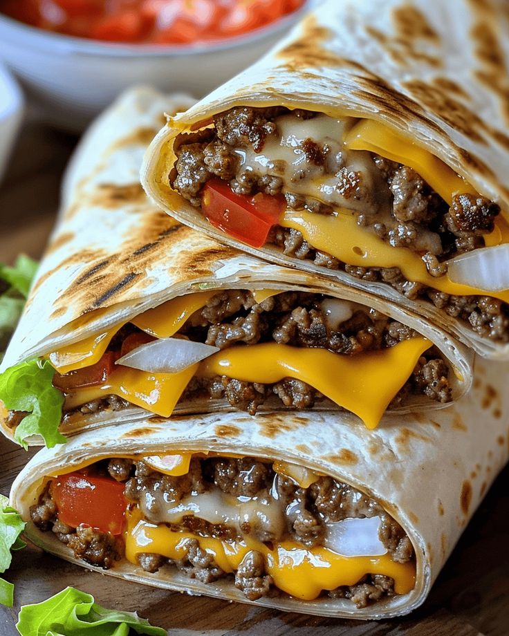 two burritos on a cutting board with lettuce, tomato and cheese