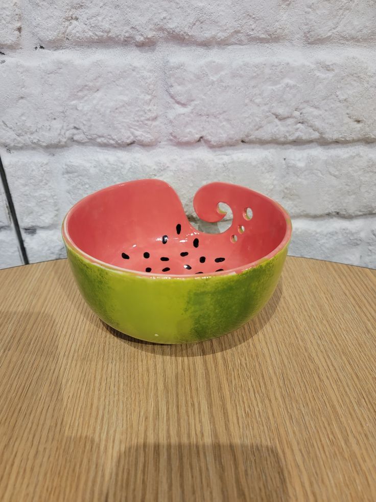 a green and pink bowl sitting on top of a wooden table next to a brick wall