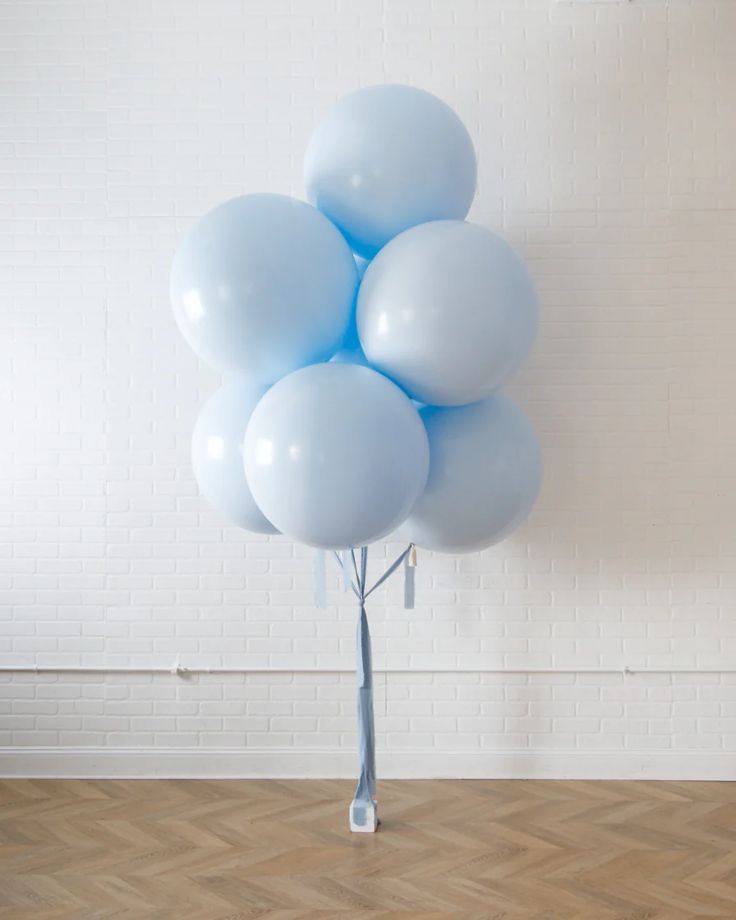 a bunch of blue balloons in a vase on a wooden floor next to a white brick wall