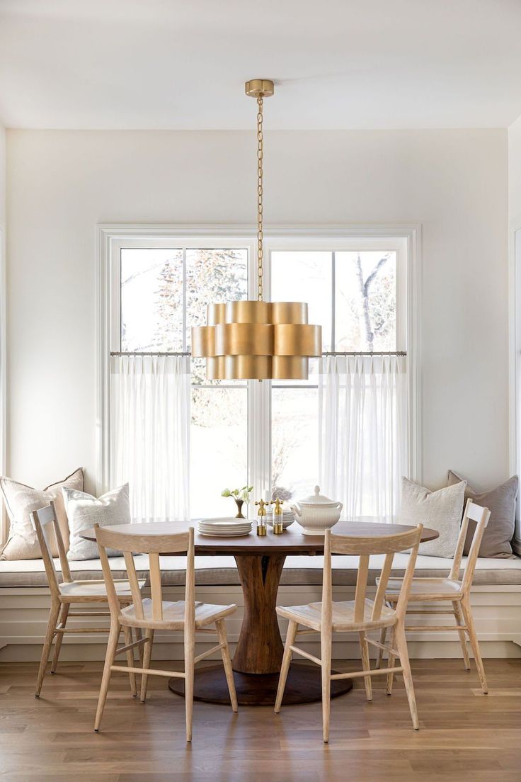 a dining room table with four chairs and a bench in front of the window,