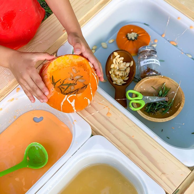 a child's hands holding an orange in front of some bowls and spoons