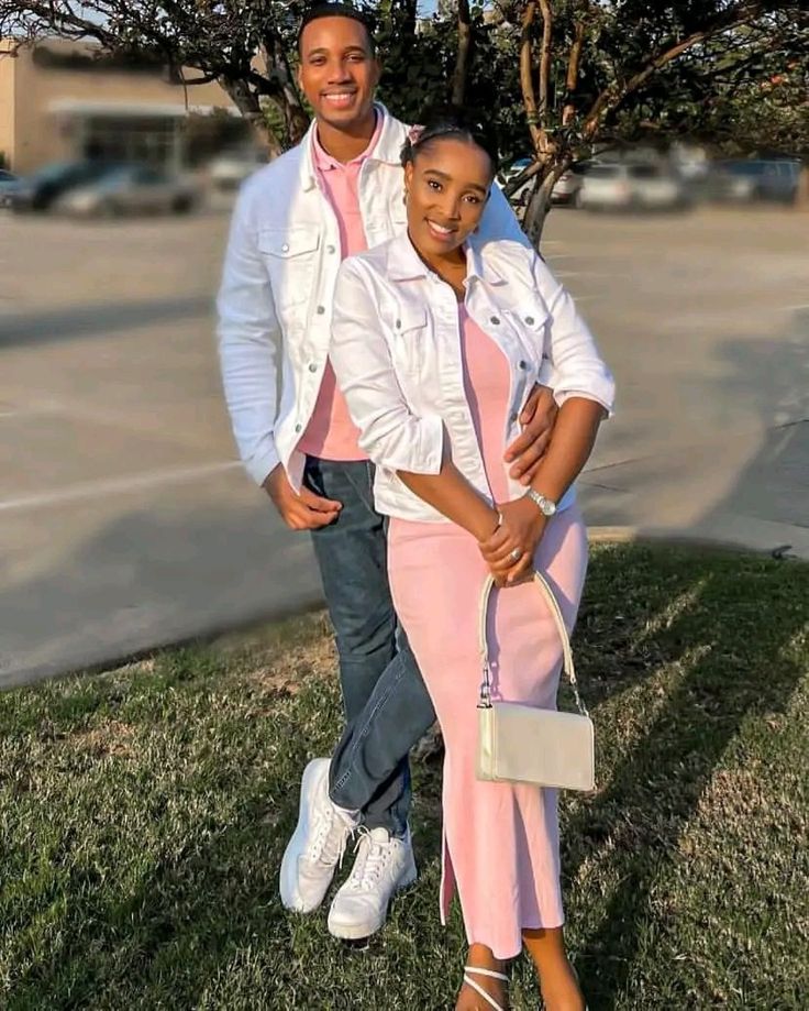 a man and woman standing next to each other in front of a tree on the grass