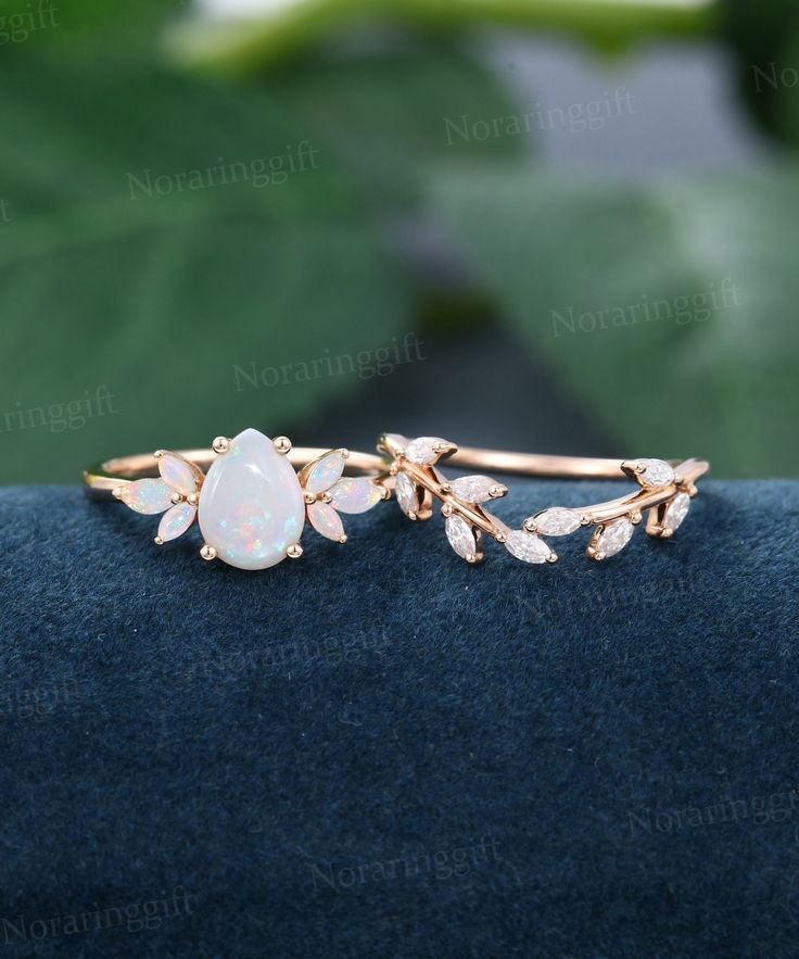 a white opal and diamond ring on top of a blue velvet surface with green leaves