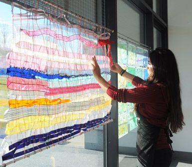 a woman is looking at an art piece hanging on the window sill in front of her