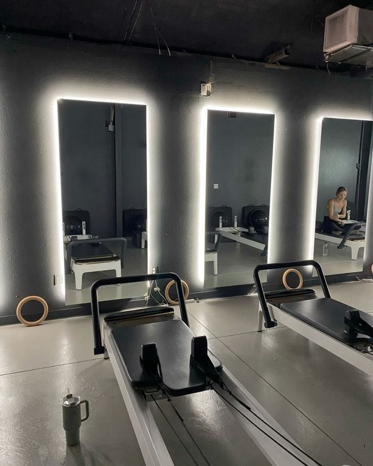 an empty room with mirrors and benches in front of the mirror is a woman sitting on a bench