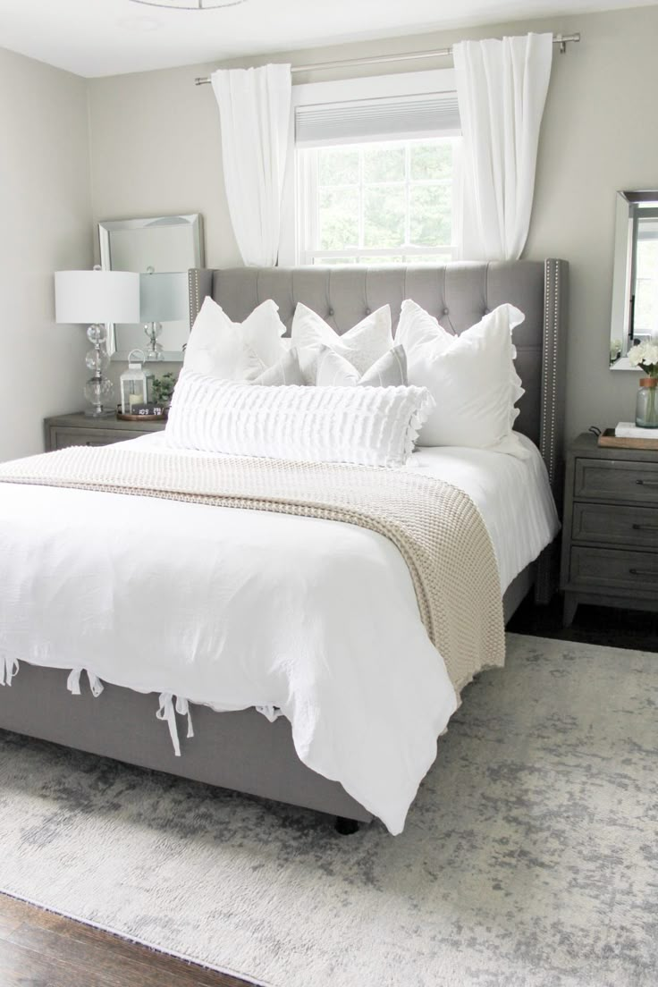 a bed with white linens and pillows in a large room next to a window